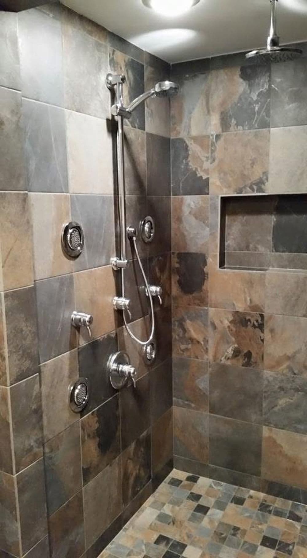 Modern shower with multi-functional faucets and tiled walls in earthy tones.