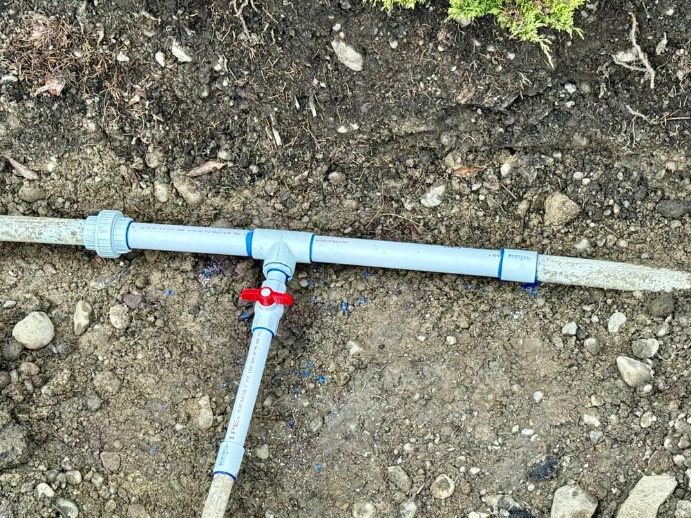 PVC irrigation pipe with a valve and fittings on bare ground, showcasing plumbing details.