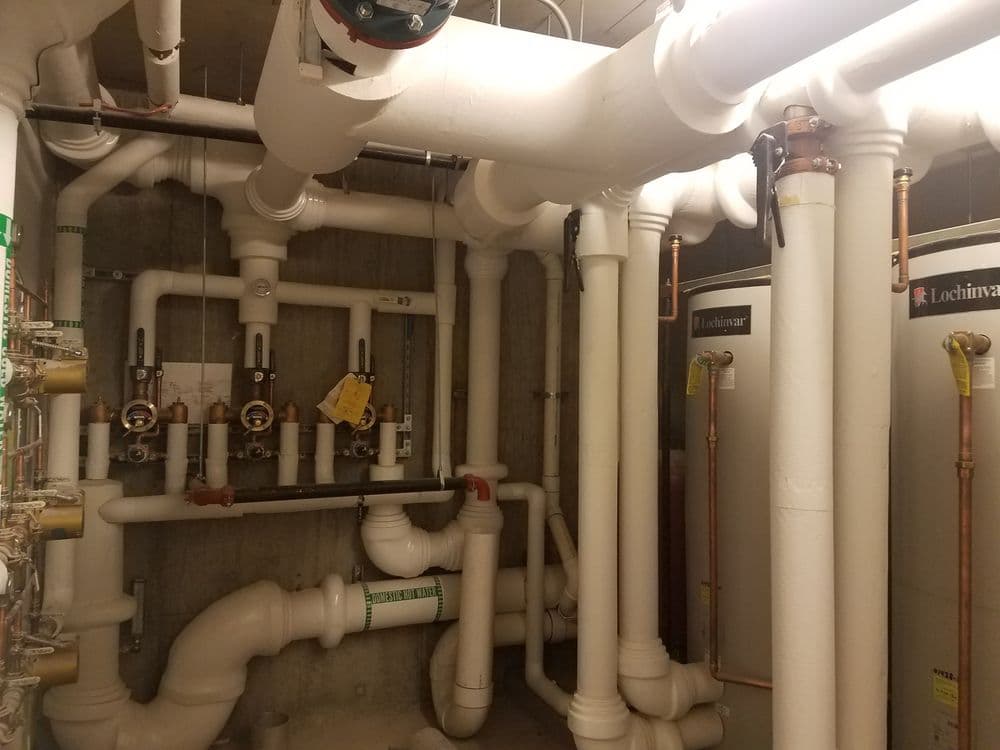 Industrial plumbing system with pipes and water heaters in a utility room.
