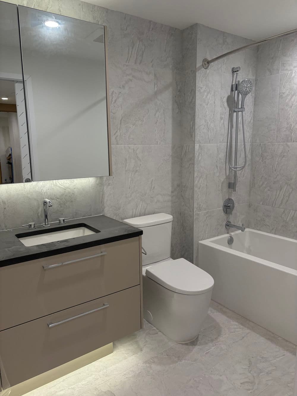 Modern bathroom featuring a bathtub, toilet, sink, and wall mirror with gray marble tiles.