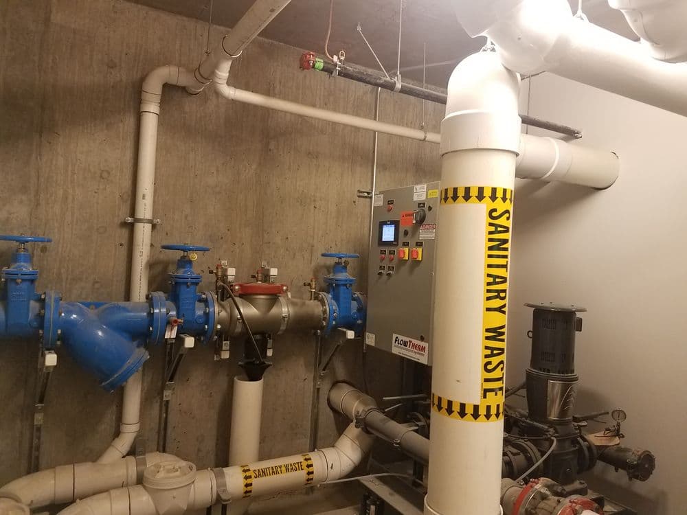 Sanitary waste plumbing system with blue valves and control panel in a utility room.