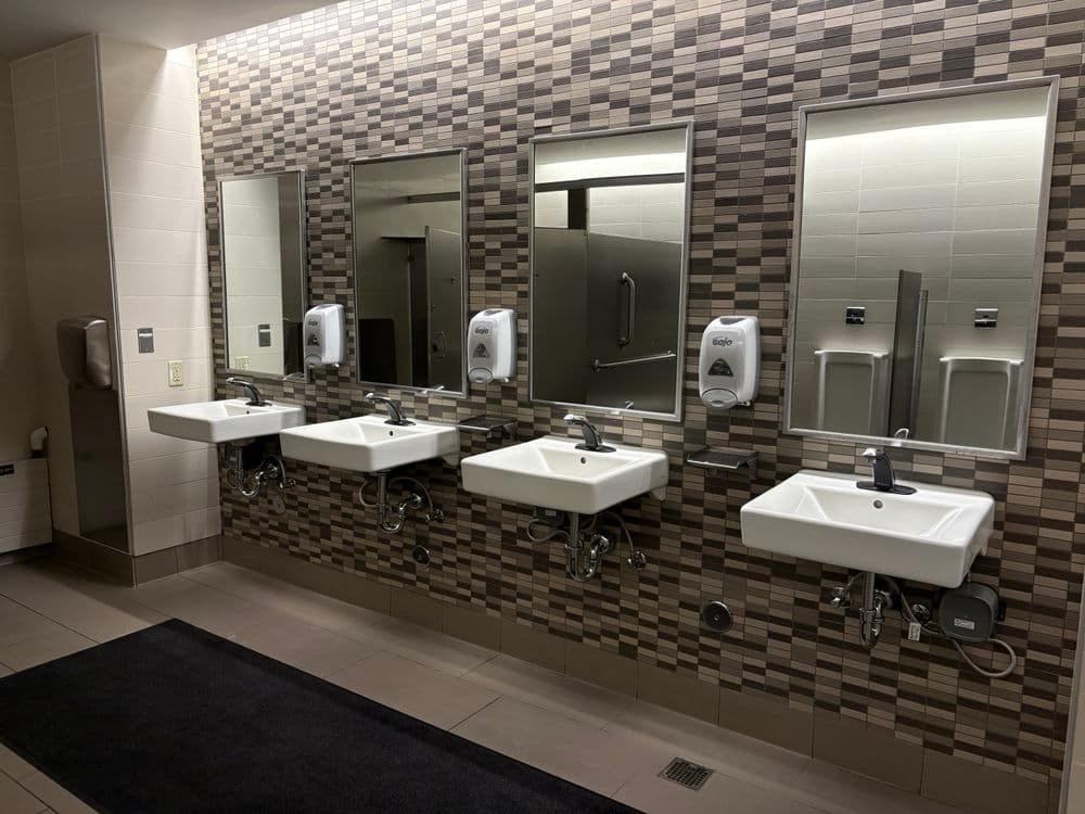 Modern restroom featuring four sinks, mirrors, and hand dryers against a textured wall.
