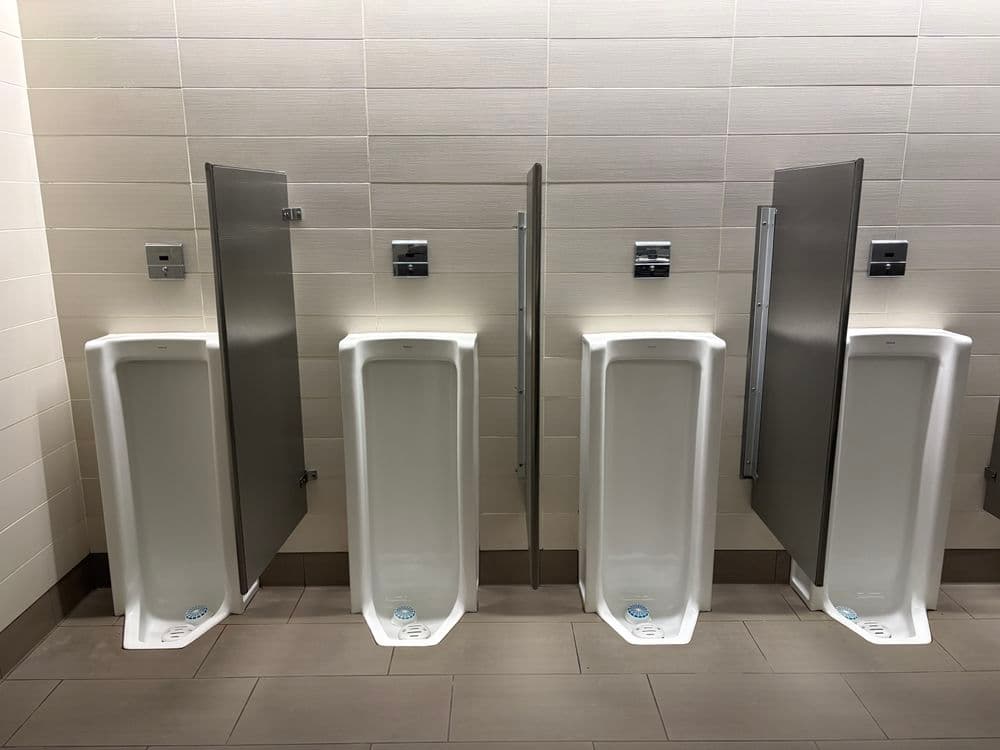 Men's restroom with four urinals and privacy dividers in a modern facility.