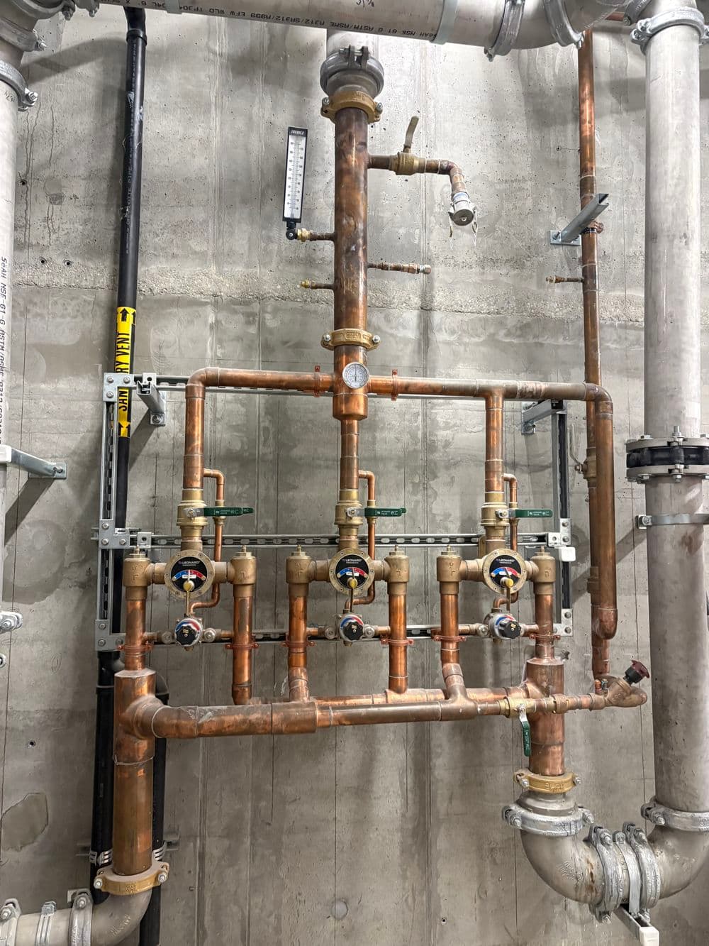 Copper plumbing system with valves and gauges against a concrete wall.