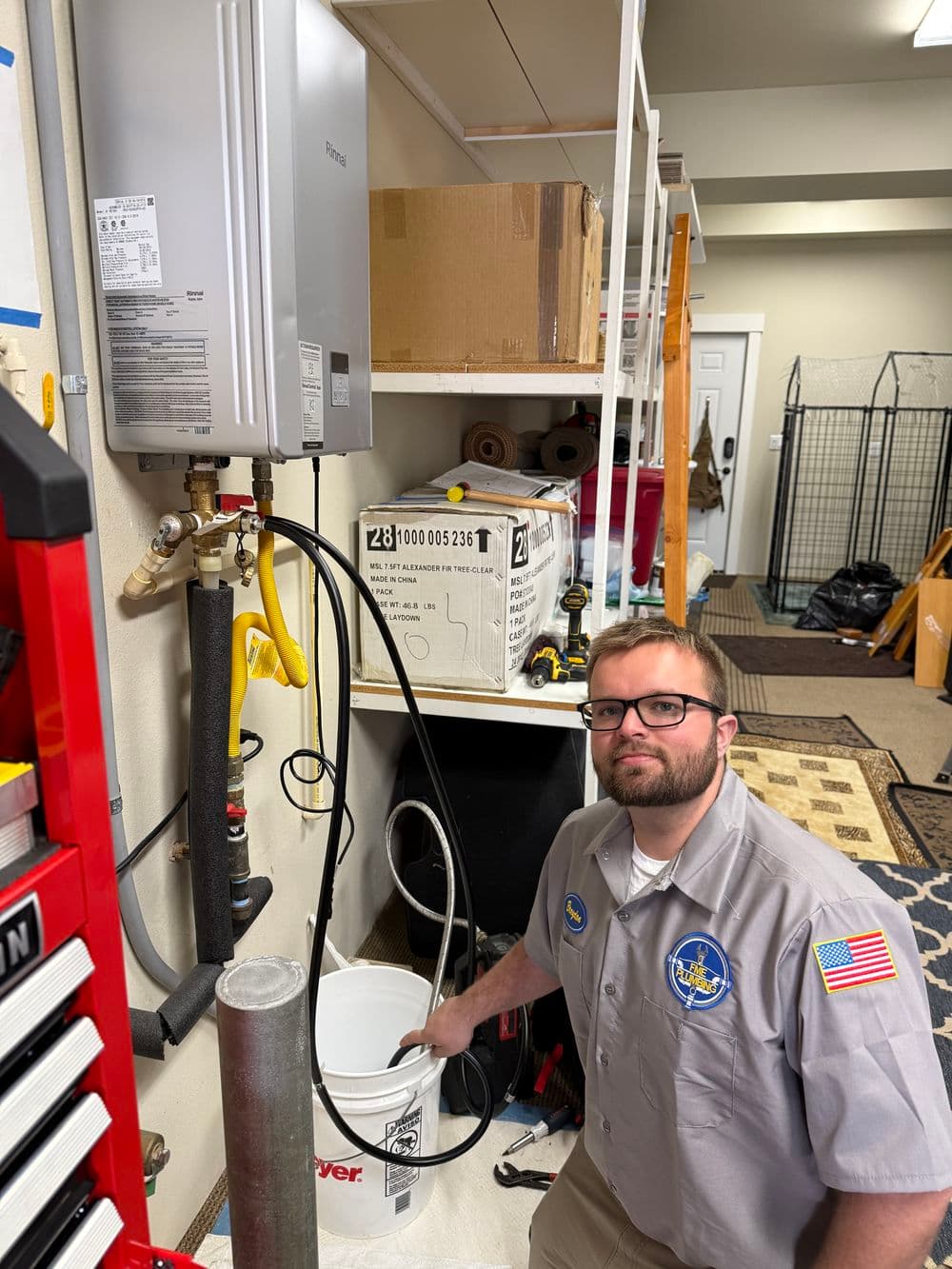 Plumber demonstrating water heater maintenance in a garage with tools and equipment.