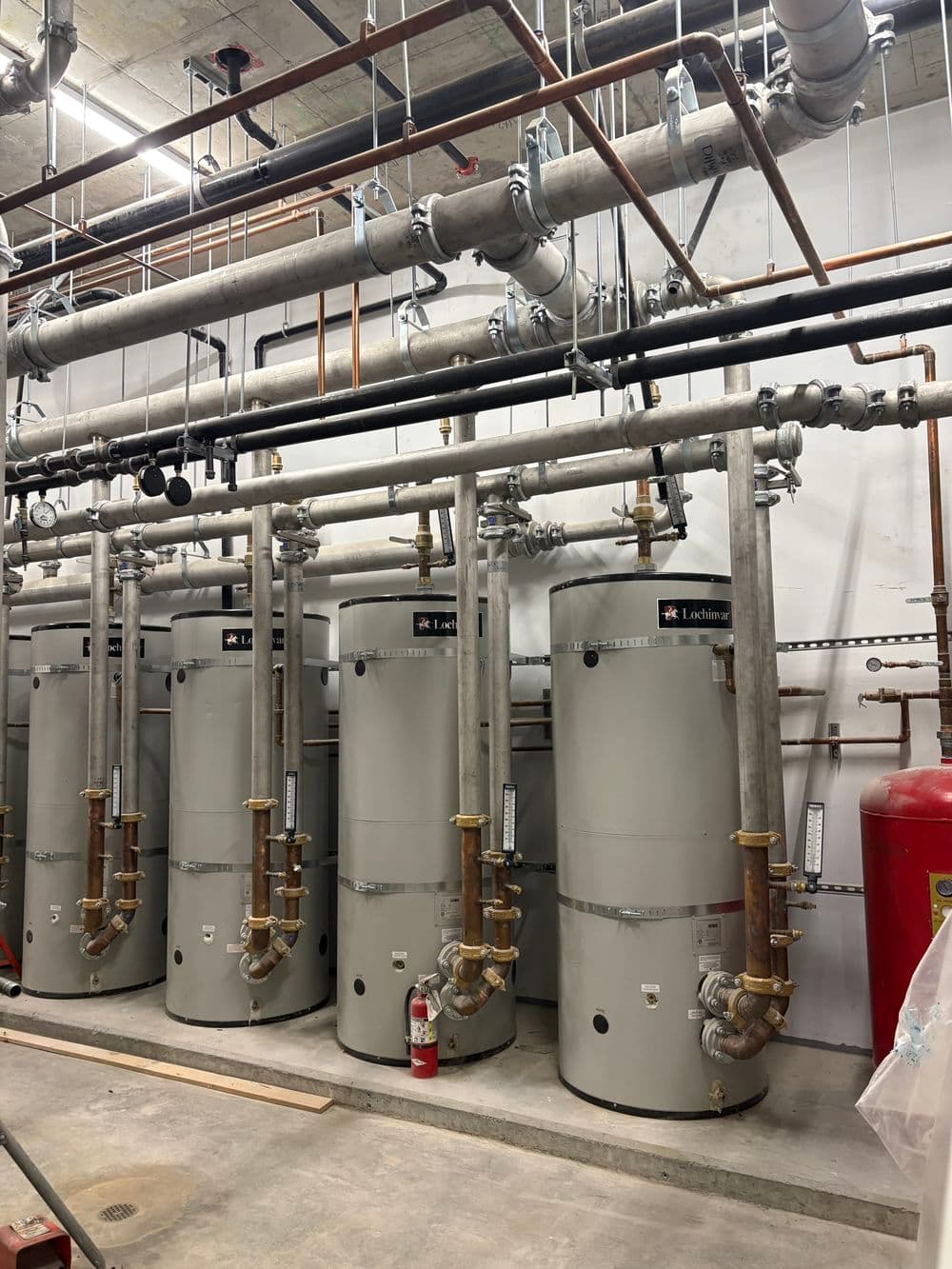 Industrial water heaters in a plumbing system with visible pipes and fire safety equipment.